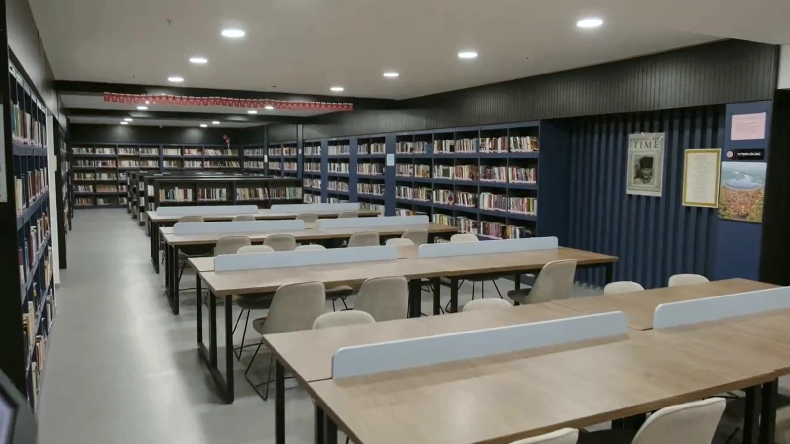Raflarıyla ve okuma masalarıyla tamamlanmış kütüphane salonu.